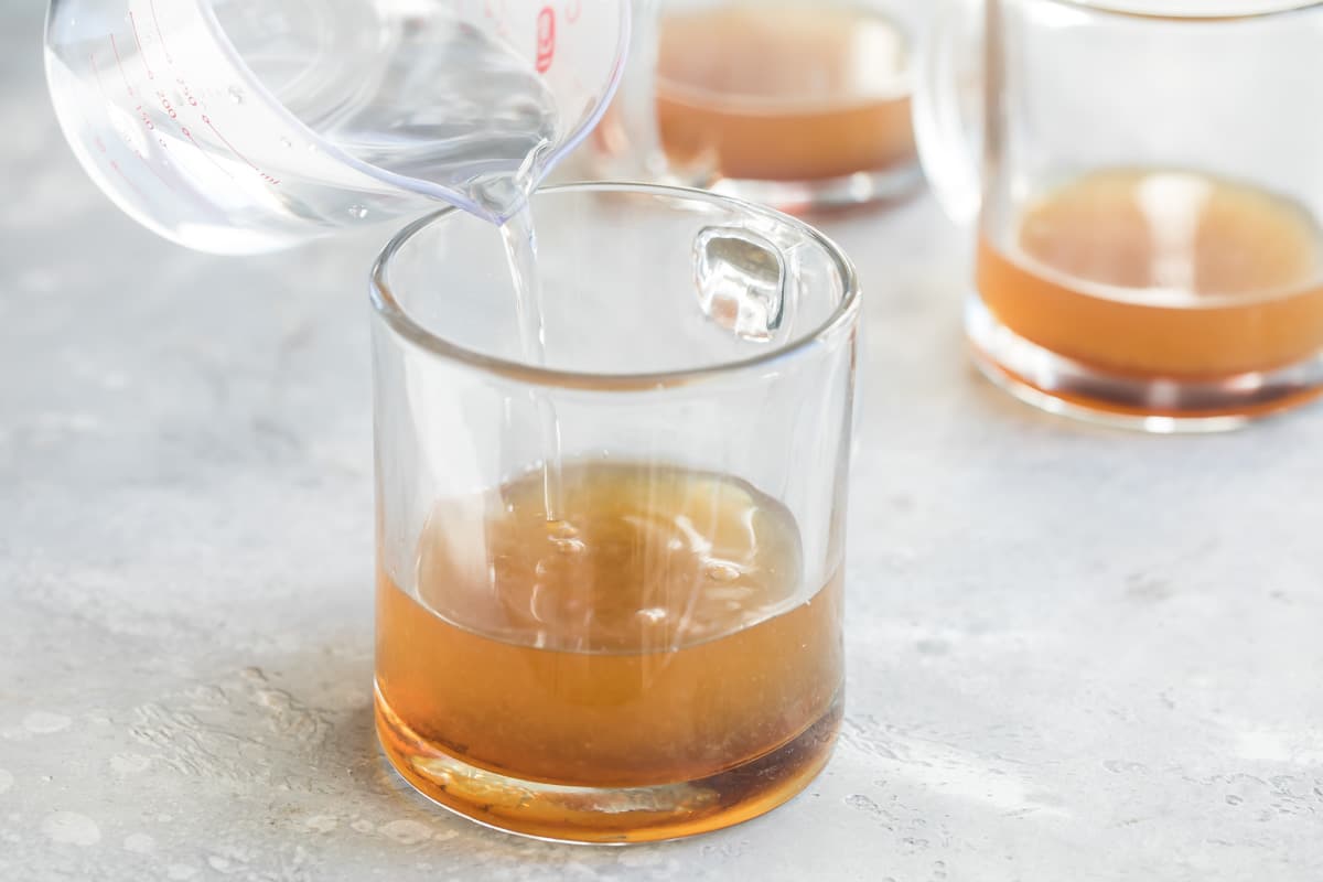 Water being poured into a clear mug with whisky.
