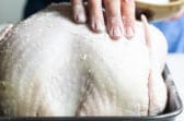 A raw turkey with salt being rubbed on it for briniing.
