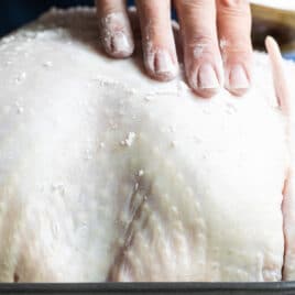 A raw turkey with salt being rubbed on it for briniing.