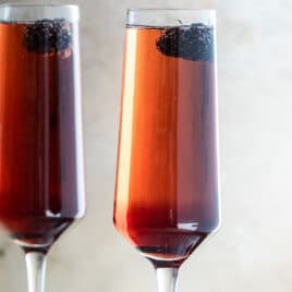 Two Kir Royale cocktails in champagne flutes on a metal tray.