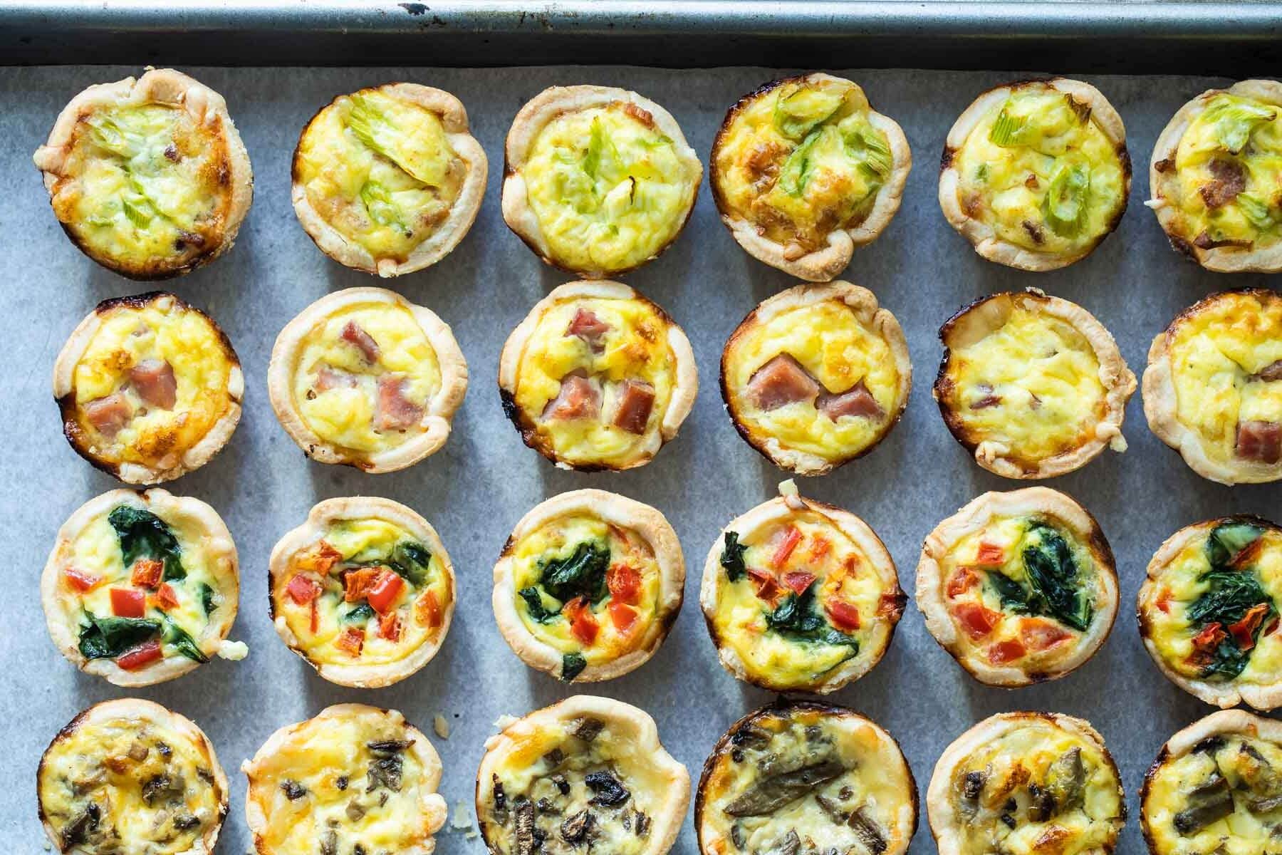A baking sheet with mini quiche arranged on it.
