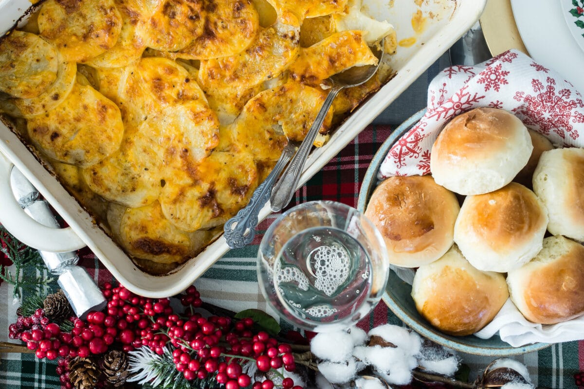 A Christmas table with scalloped potatoes and dinner rolls on it.