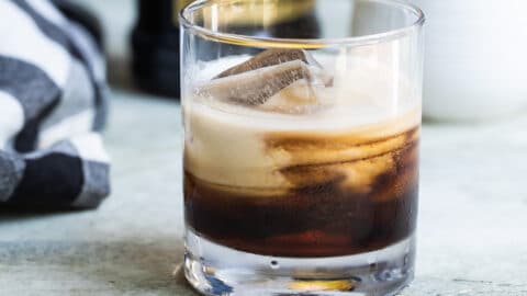 A white Russian cocktail with a bottle of Kahlua in the background.