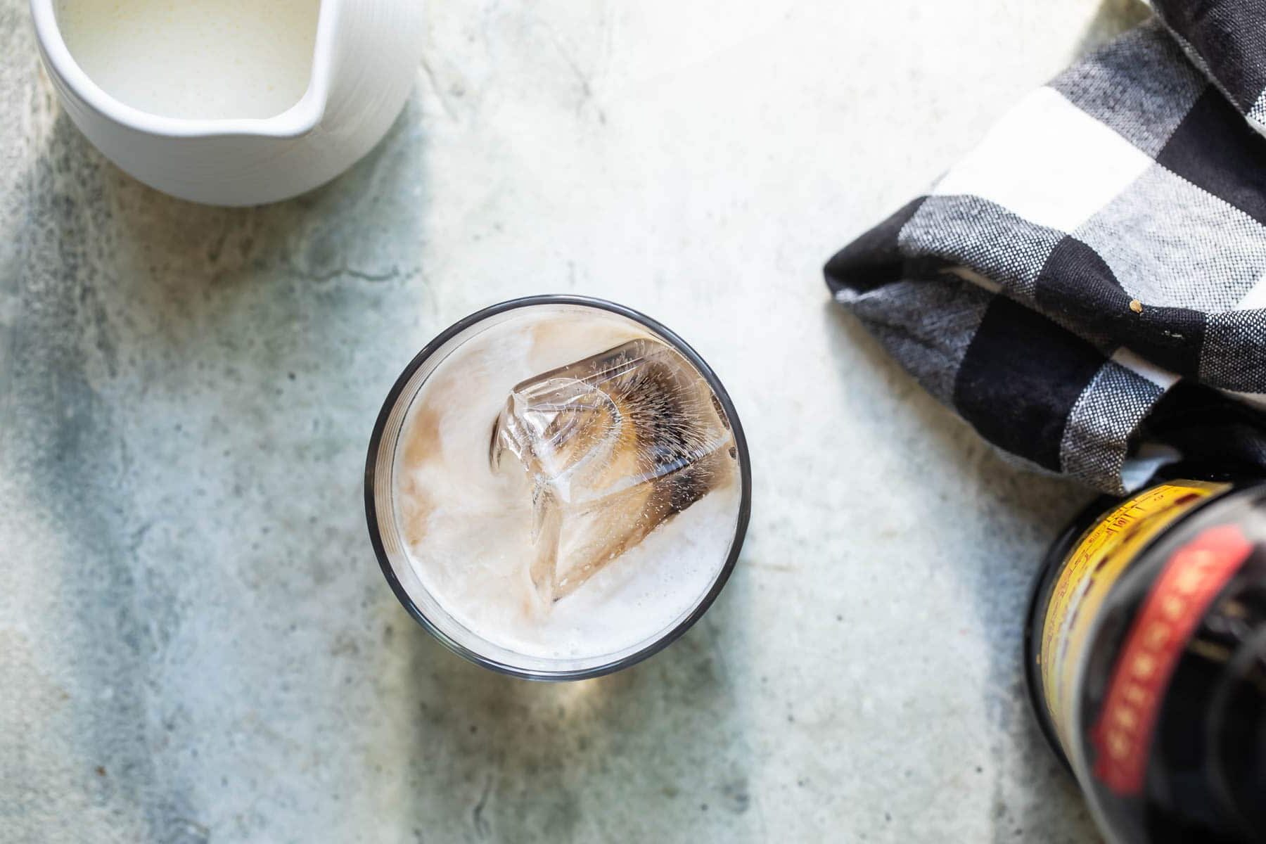 A white Russian cocktail with a bottle of Kahlua in the background.