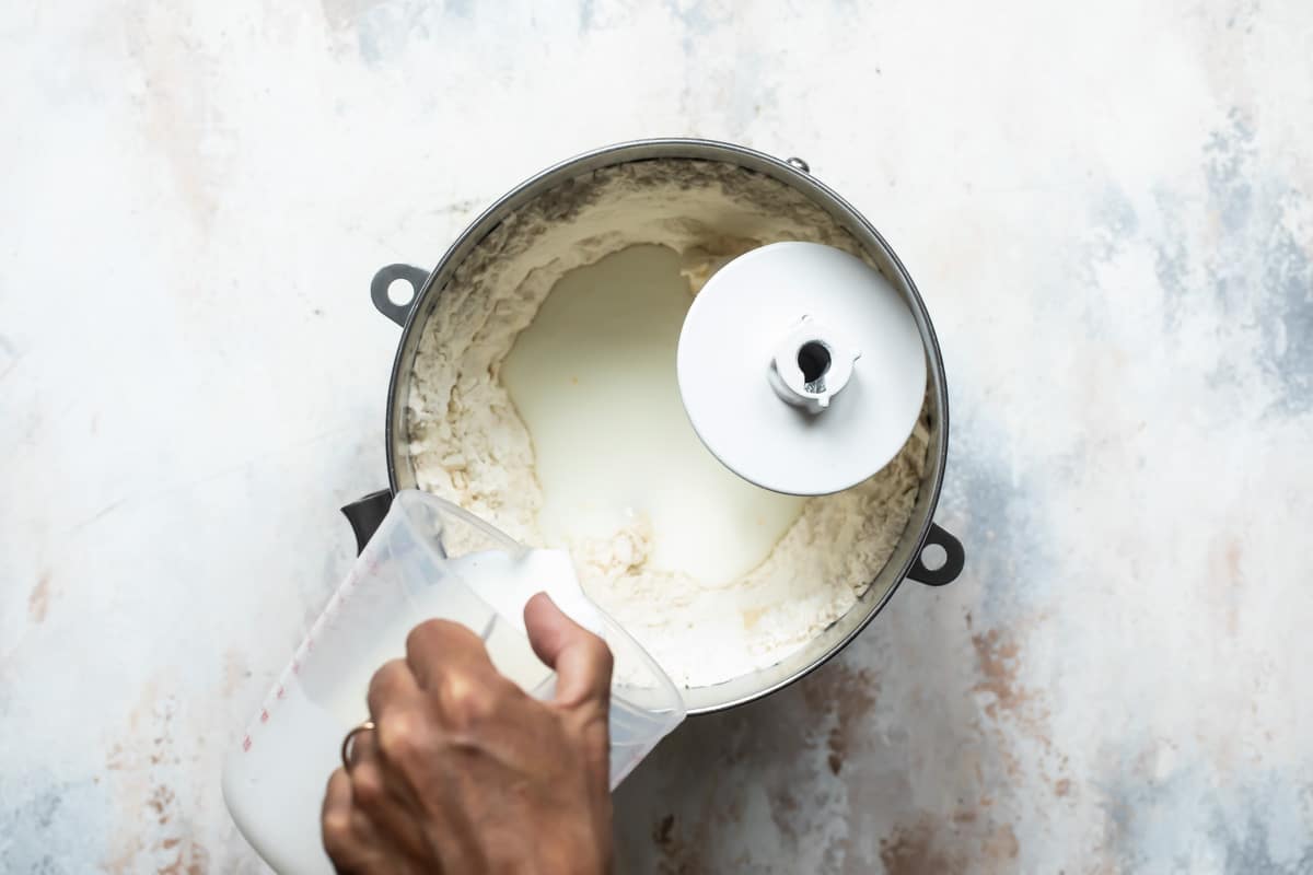 White liquid being poured into a silver mixing bowl filled with dough.