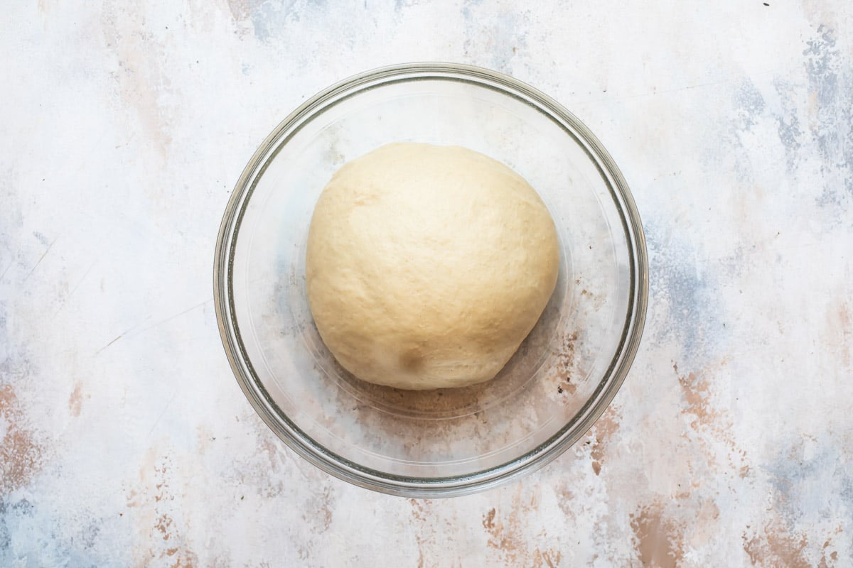 A ball of dough in a clear glass bowl.