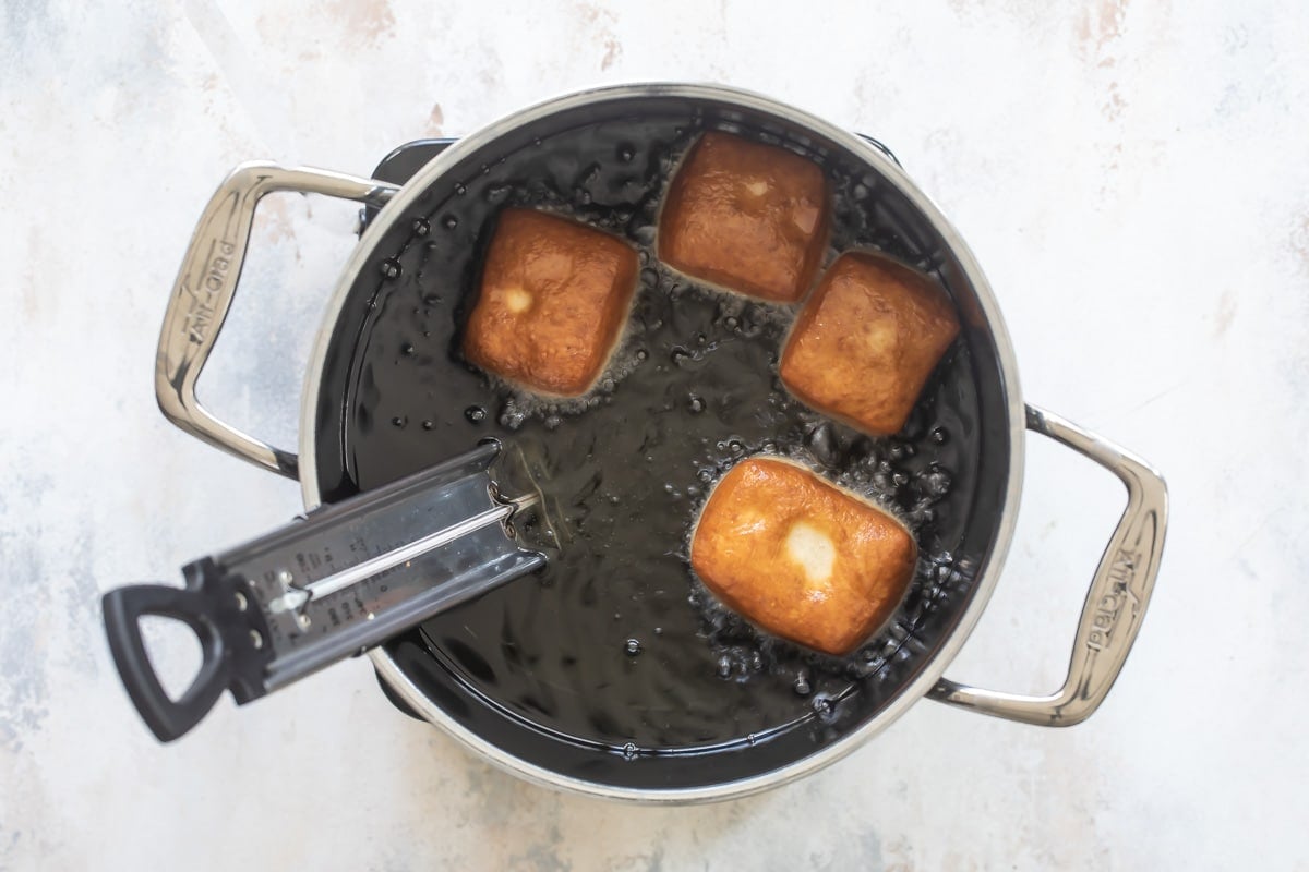 Four beignets being fried in oil.
