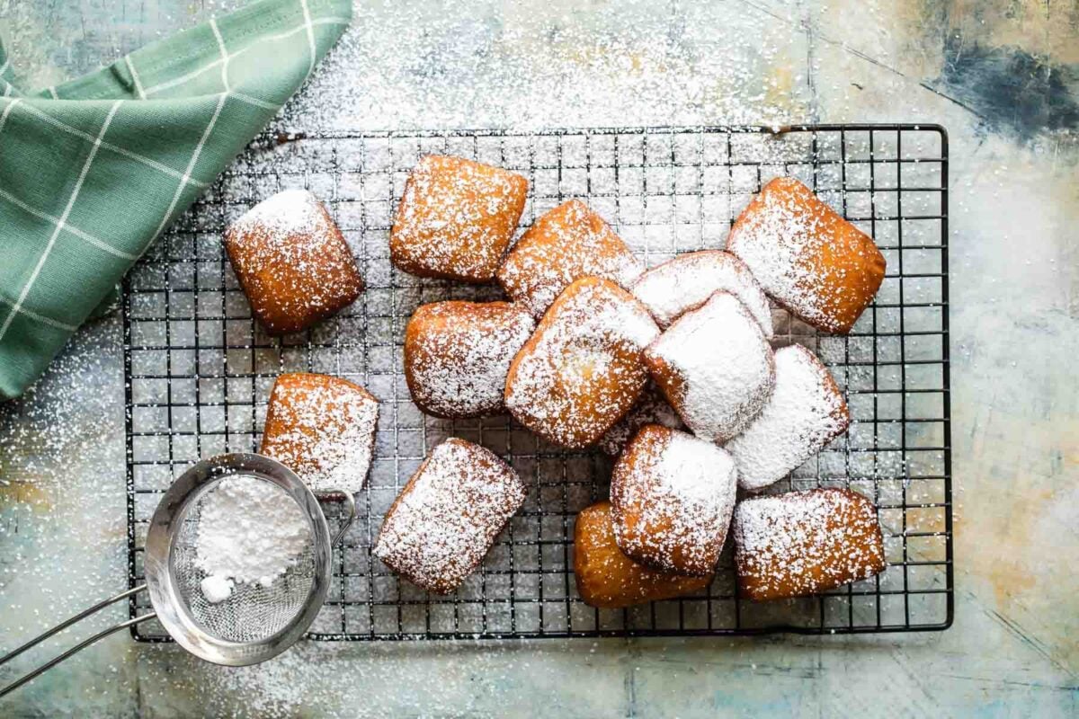 Beignets on a cooling rack with powdered sugar sprinkled on top.