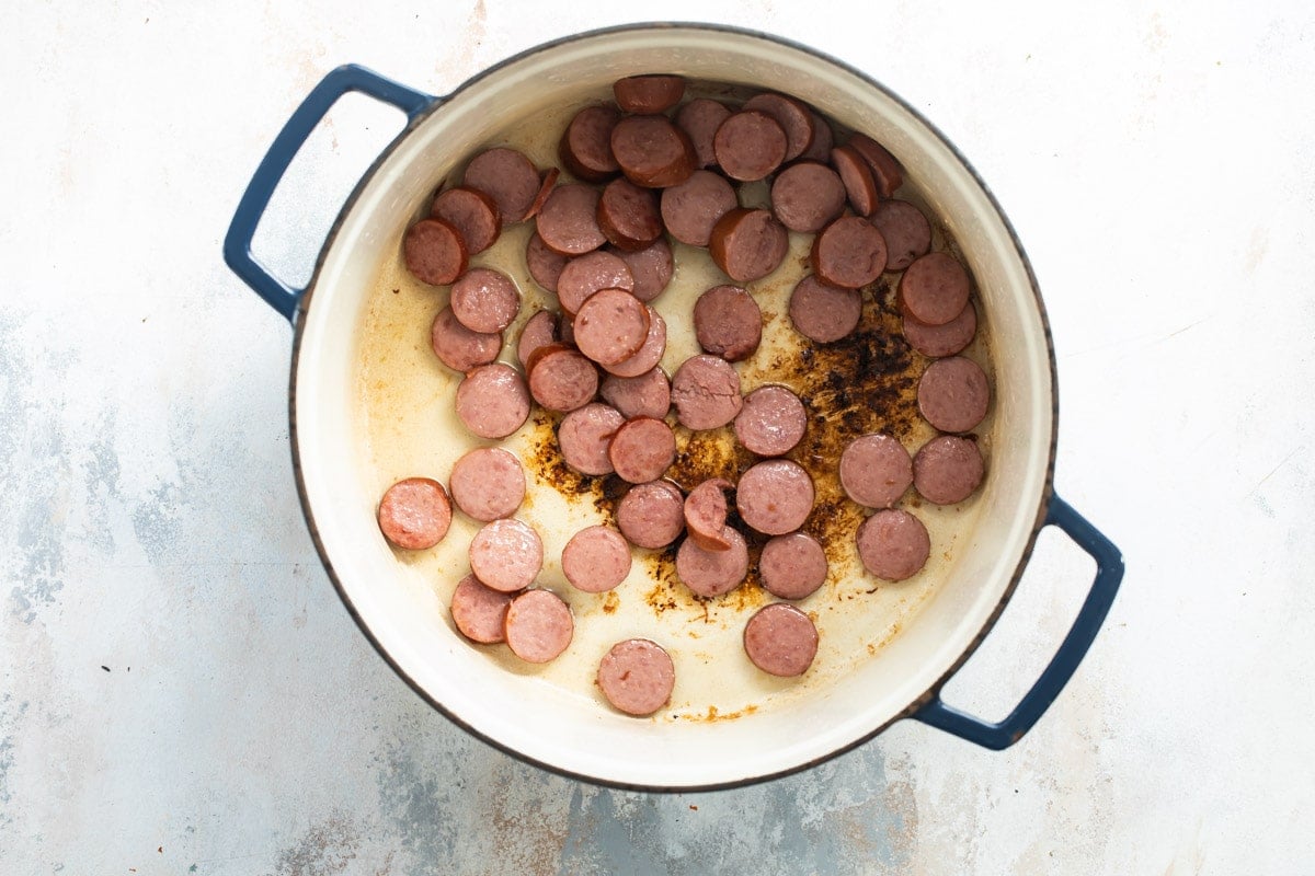 Andouille sausages being cooked in a Dutch oven.