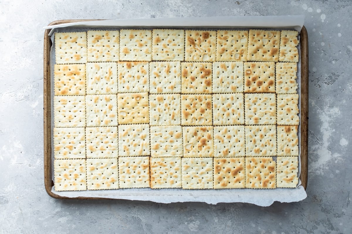 Saltine crackers lining a parchment paper lined baking sheet.