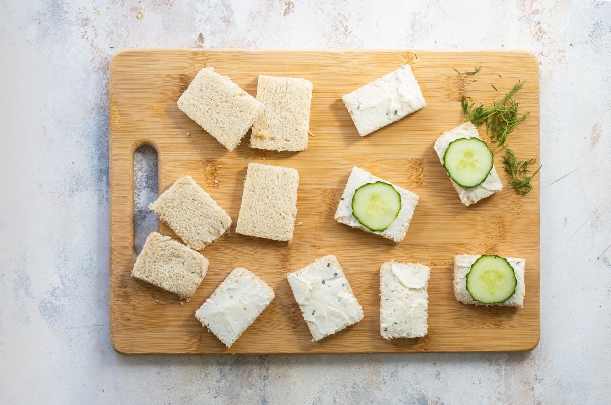 Cucumber sandwiches being assembled on a wooden cutting board.