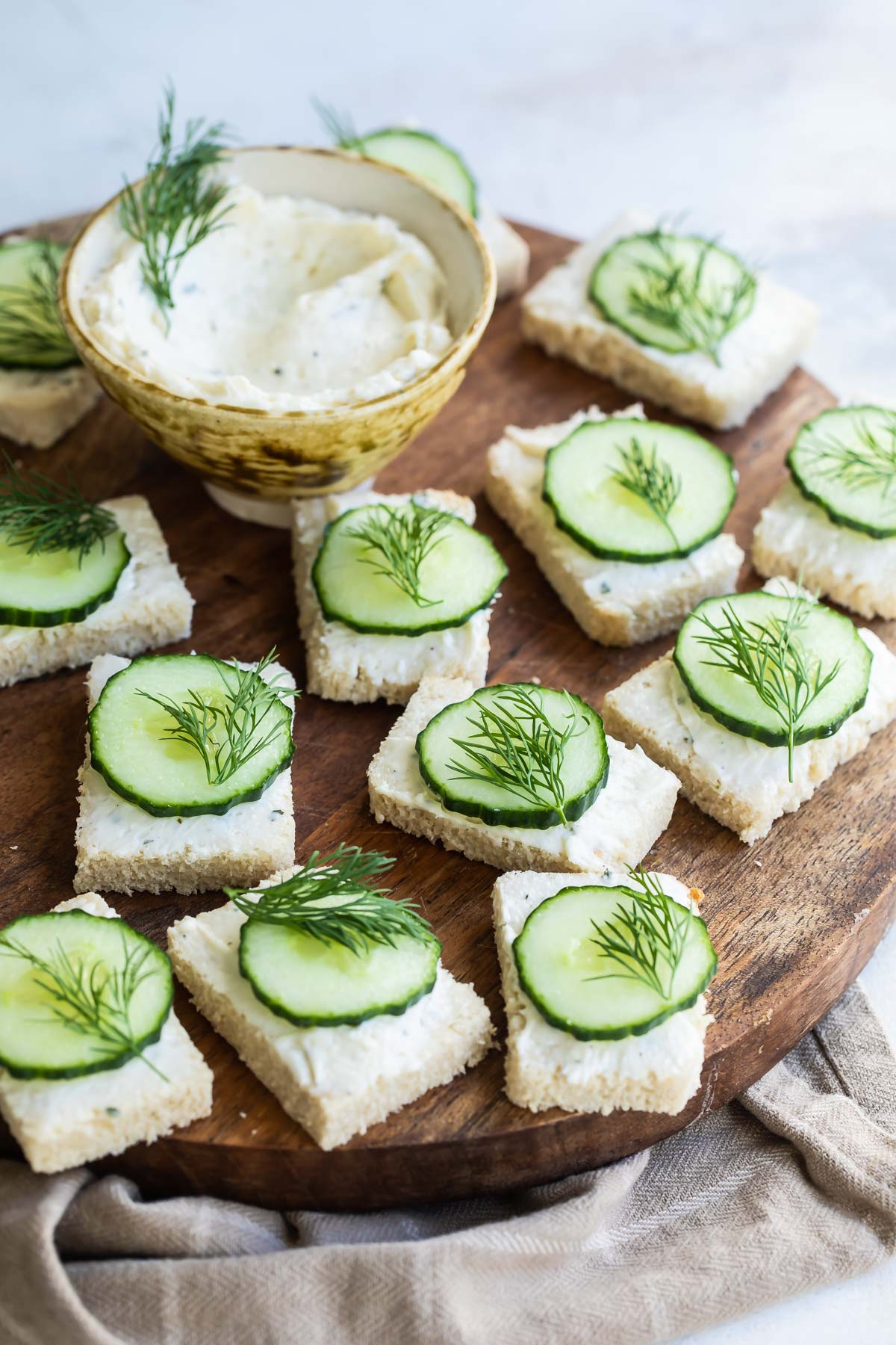 Cucumber sandwiches on a round wooden platter.