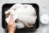 Someone patting an uncooked turkey with a paper towel.