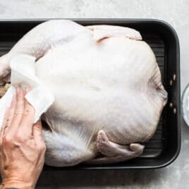 Someone patting an uncooked turkey with a paper towel.