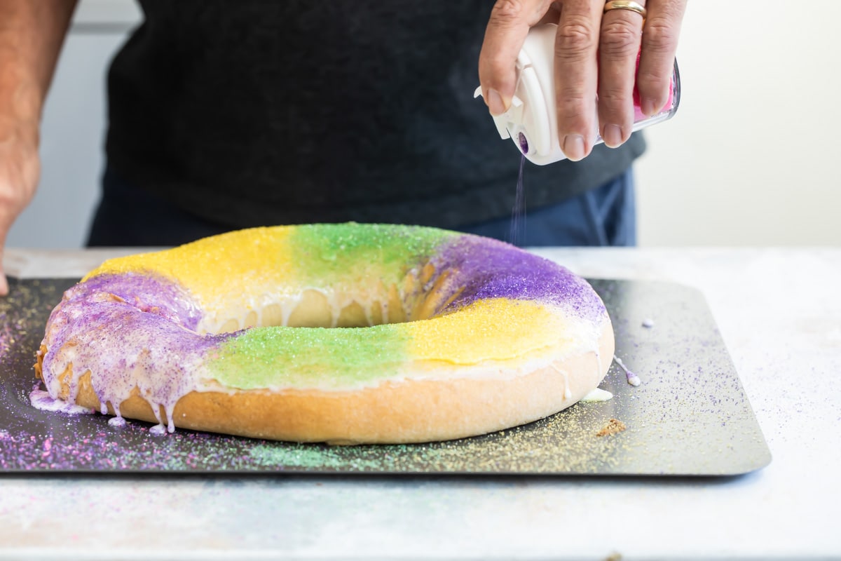 Someone sprinkling colored sugar over a king cake.