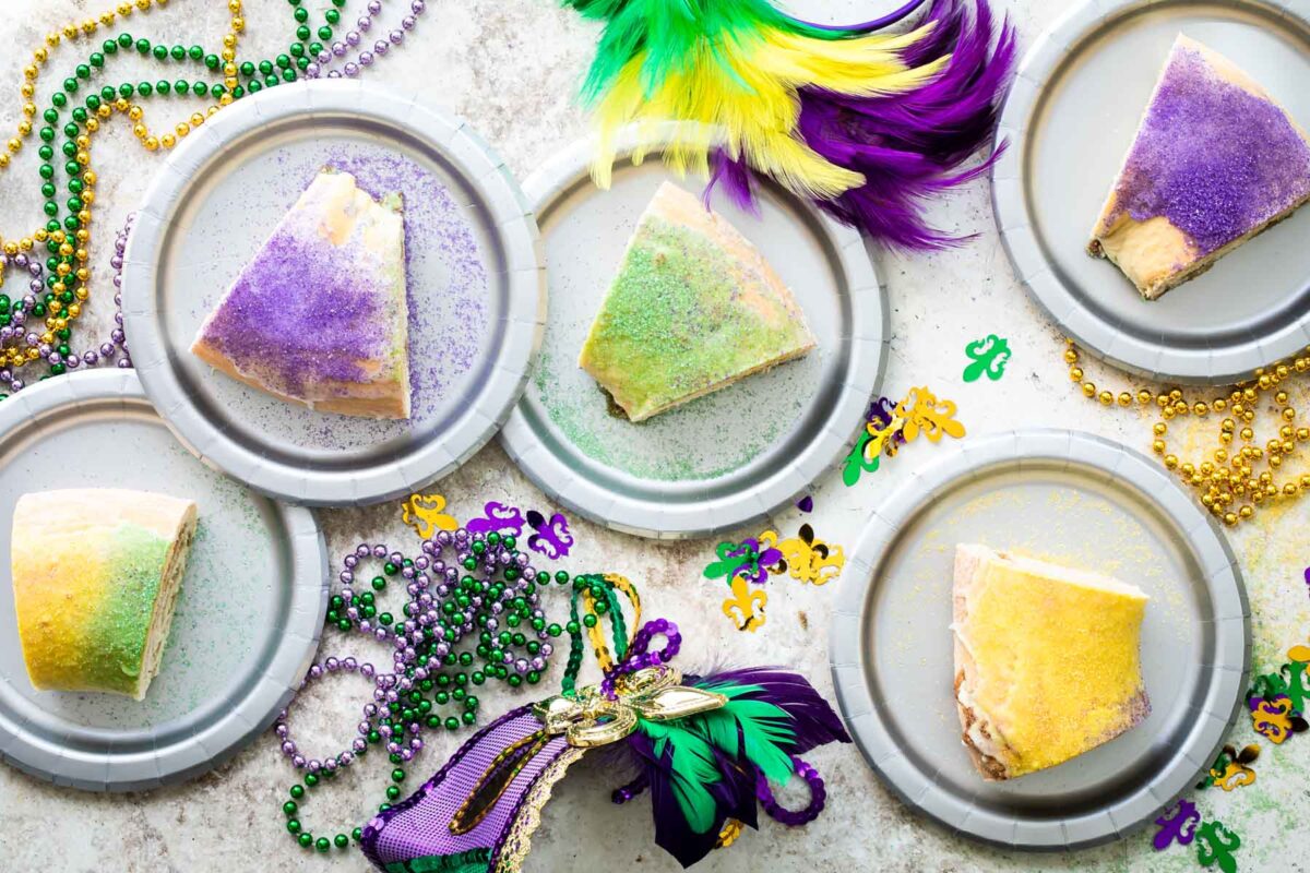 Five pieces of king cake on silver plates on a table.