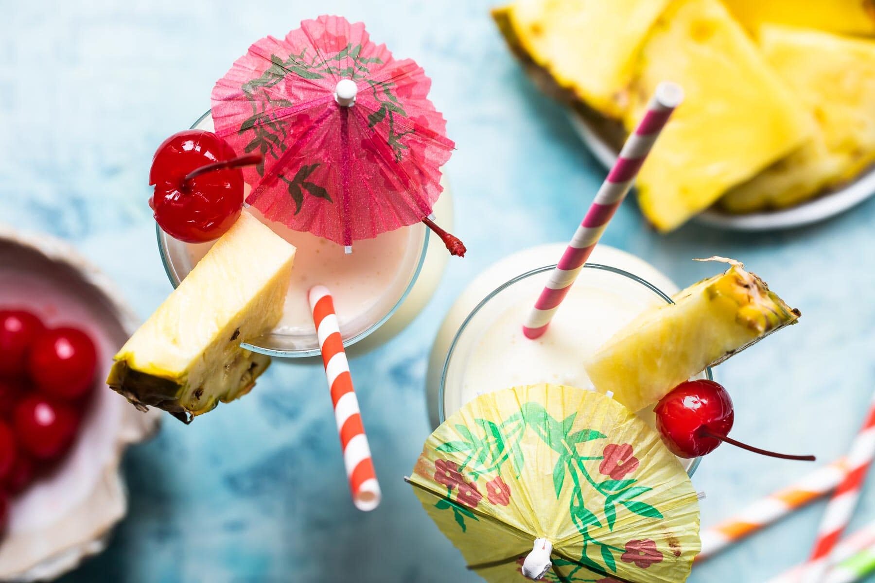 Two piña coladas garnished with pineapple and cherries.