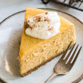 A slice of pumpkin cheesecake with whipped cream on a plate.