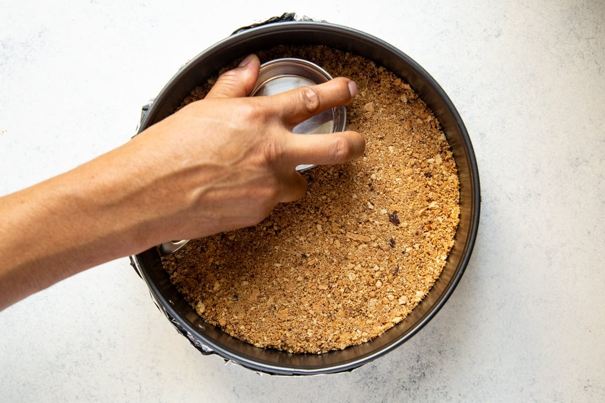 Pressing graham cracker crumbs into a springform pan.