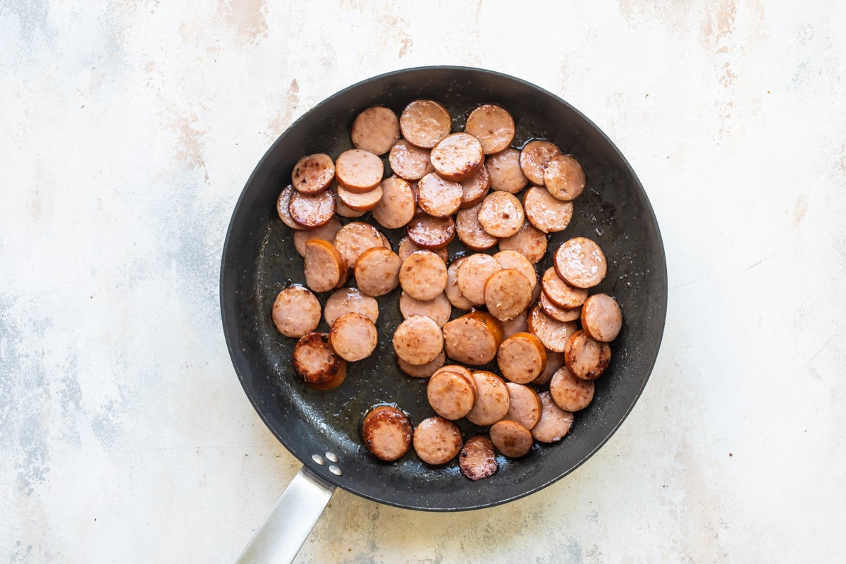 Andouille sausages being cooked in a frying pan.