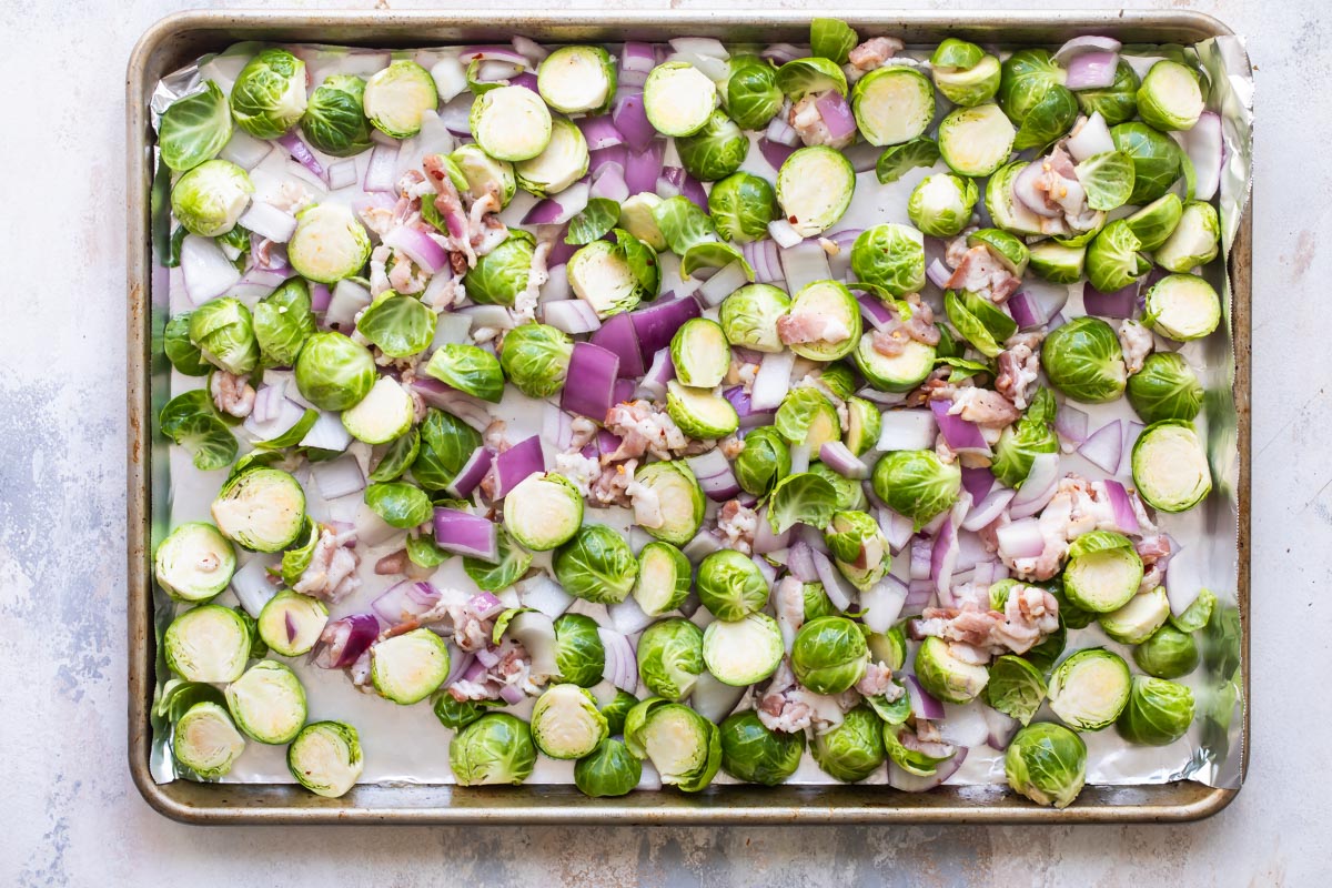 Brussels sprouts, bacon and red onion on a parchment paper lined baking sheet.