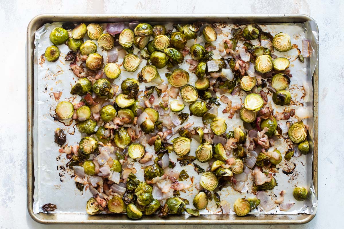 Roasted Brussels sprouts, bacon and red onion on a parchment paper lined baking sheet.