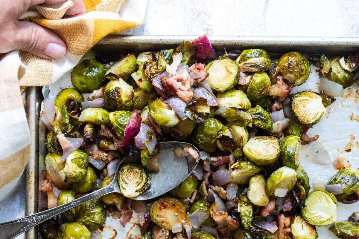 Roasted Brussels sprouts, bacon and red onion on a parchment paper lined baking sheet.