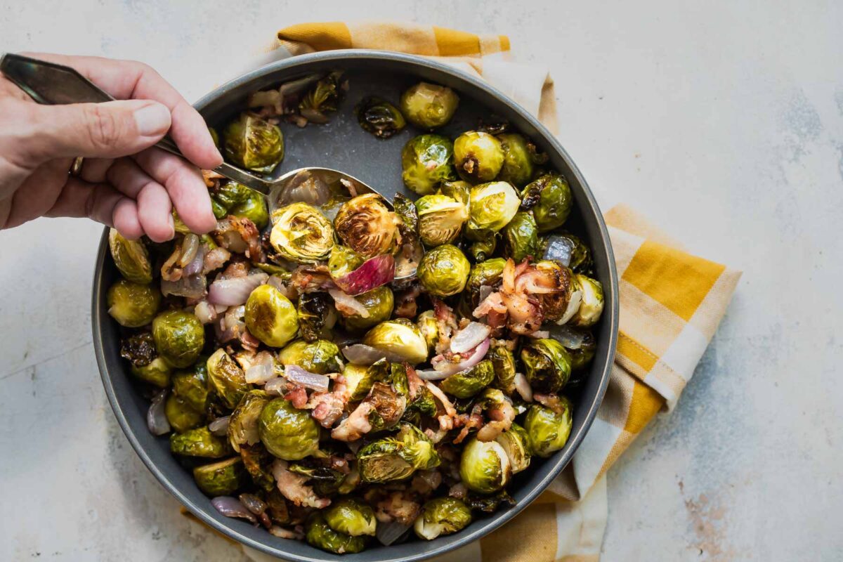 Roasted brussels sprouts being scooped out of a metal pan.