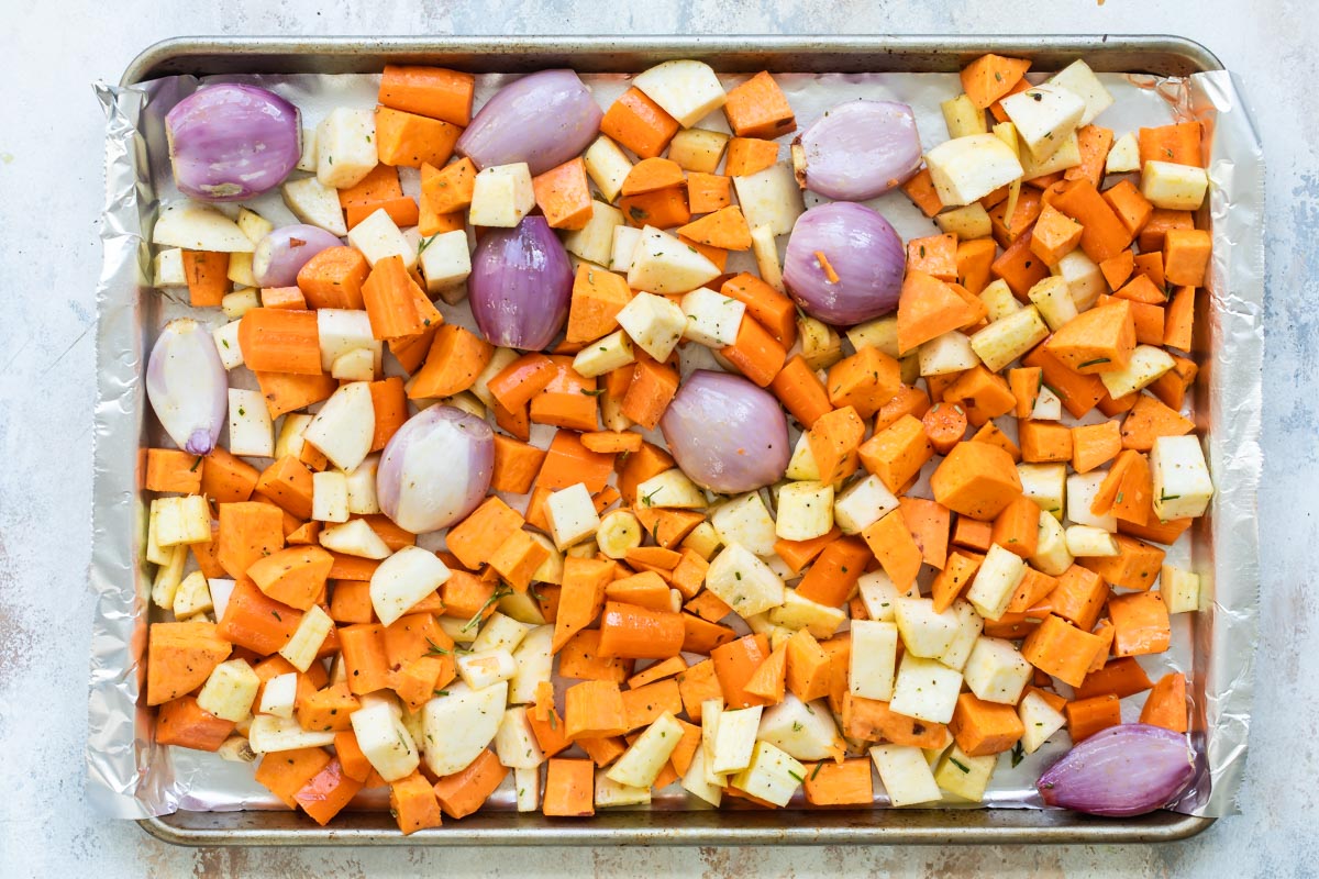 Root vegetables on a parchment paper lined baking sheet before being roasted.
