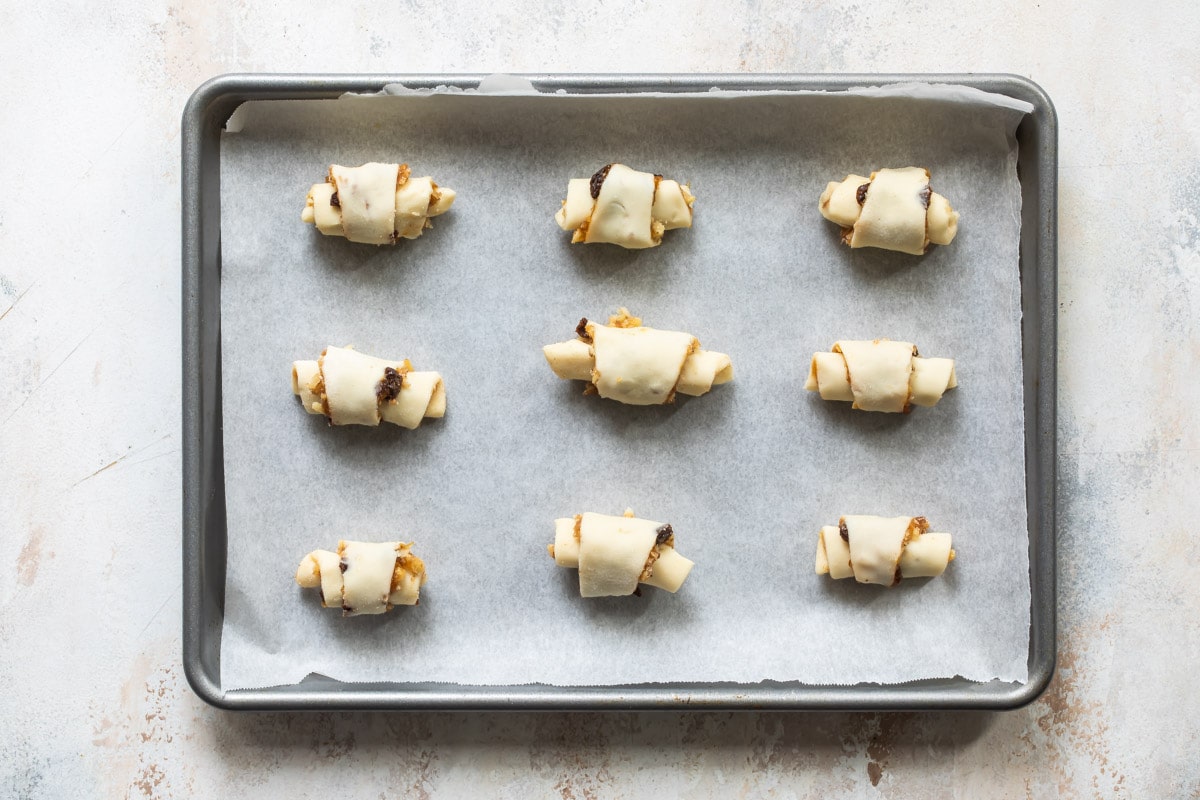 Nine unbaked rugelach on a parchment paper lined baking sheet.