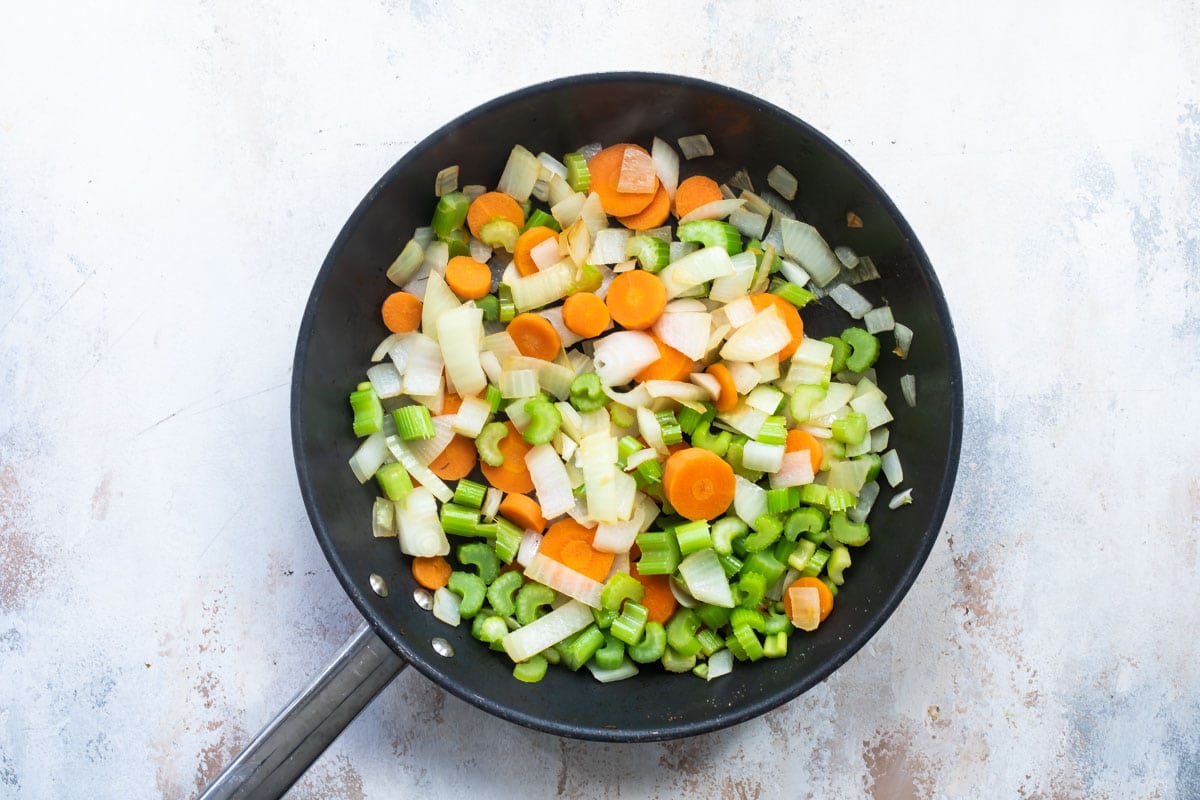 A frying pan with onion, celery and carrots in it.