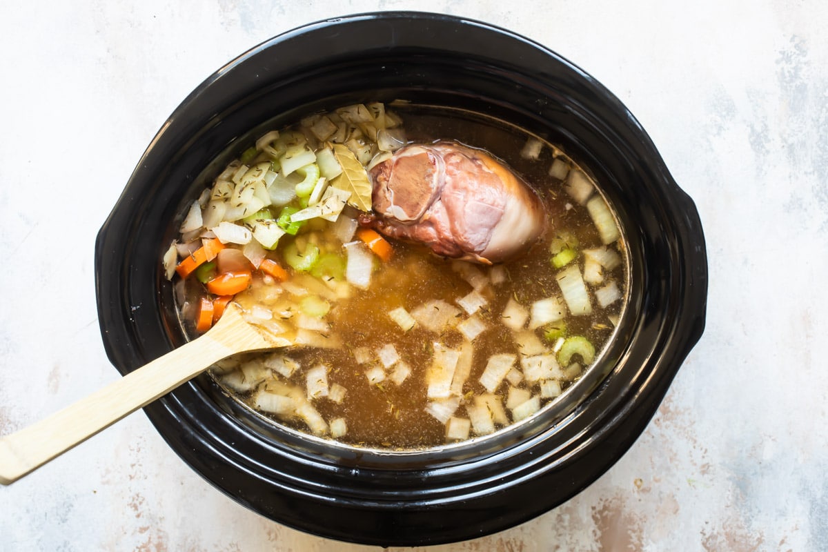 A slow cooker with uncooked ham and bean soup.