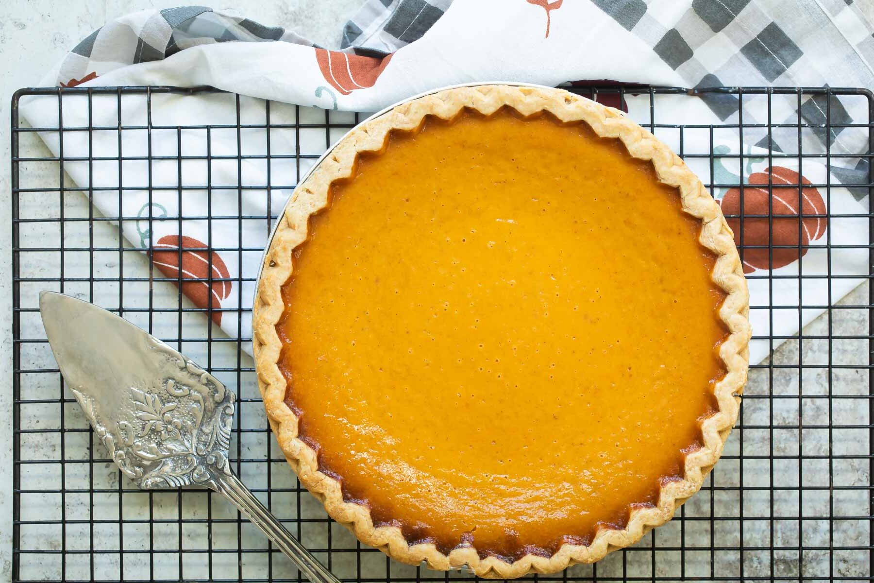 A baked pumpkin pie cooling on a wire rack.