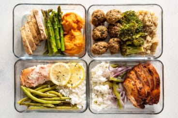 4 glass containers filled with meal prep foods like veggies, rice, chicken, and salmon.