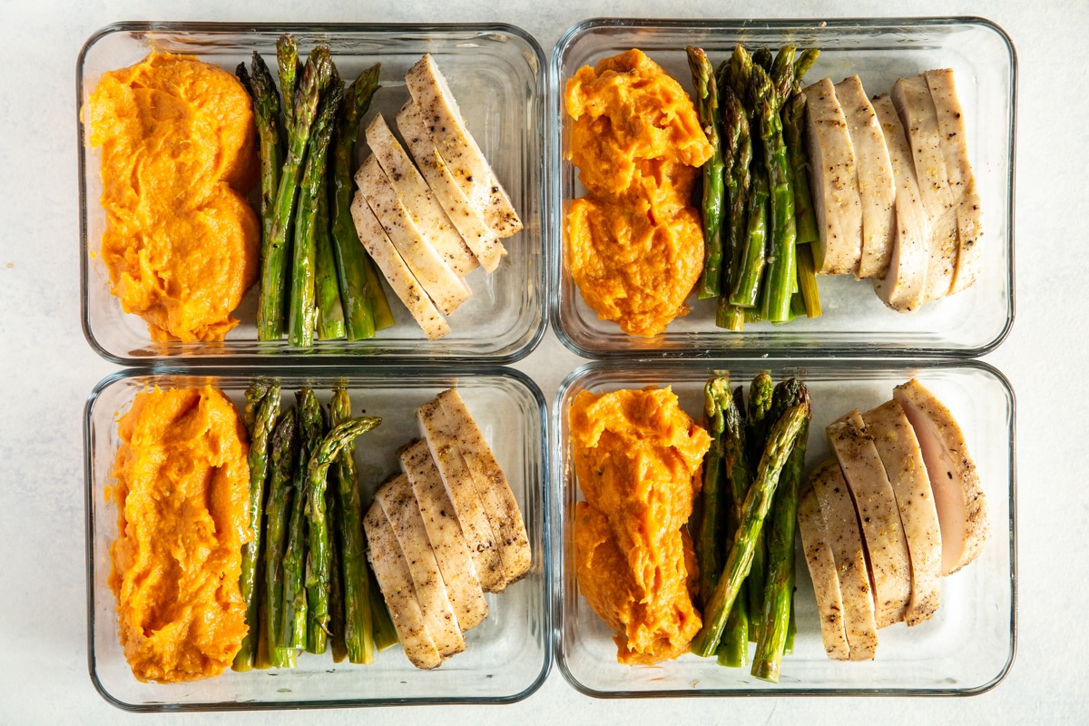 4 glass containers filled with meal prep foods like veggies, rice, chicken, and salmon.