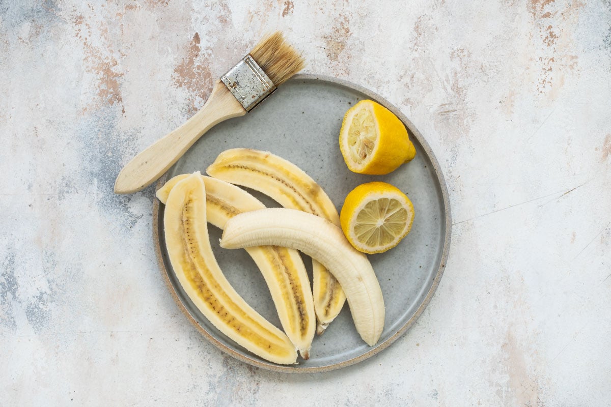 Bananas sliced lengthwise on a plate next to lemon halves.