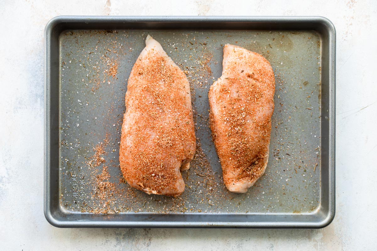 Uncooked seasoned chicken on a baking sheet.
