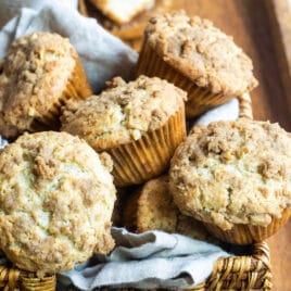 Coffee cake muffins in a basket on a wooden serving tray.