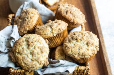 Coffee cake muffins in a basket on a wooden serving tray.