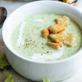 A bowl of cream of broccoli soup with croutons on top.