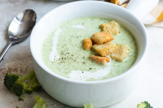 A bowl of cream of broccoli soup with croutons on top.