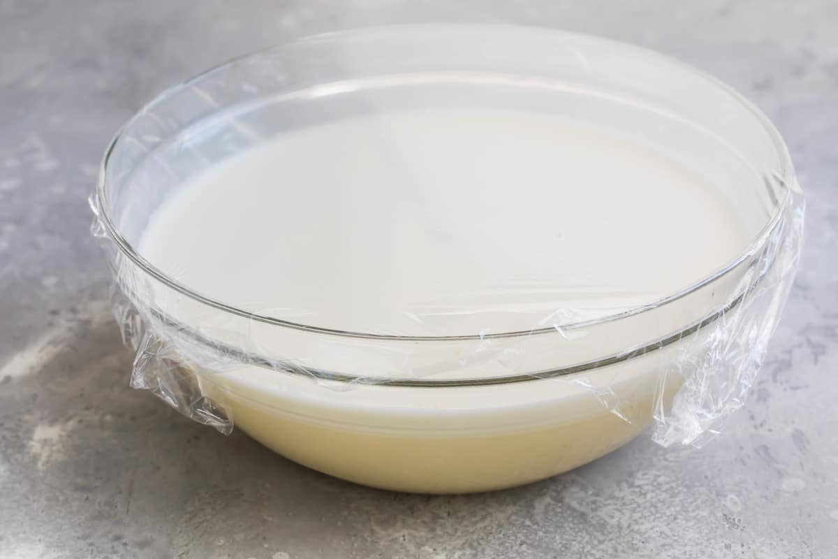 Eggnog in a clear bowl covered with plastic wrap.