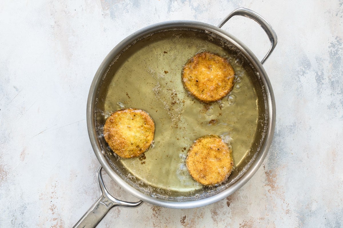 Fried green tomatoes frying in a vat of oil.