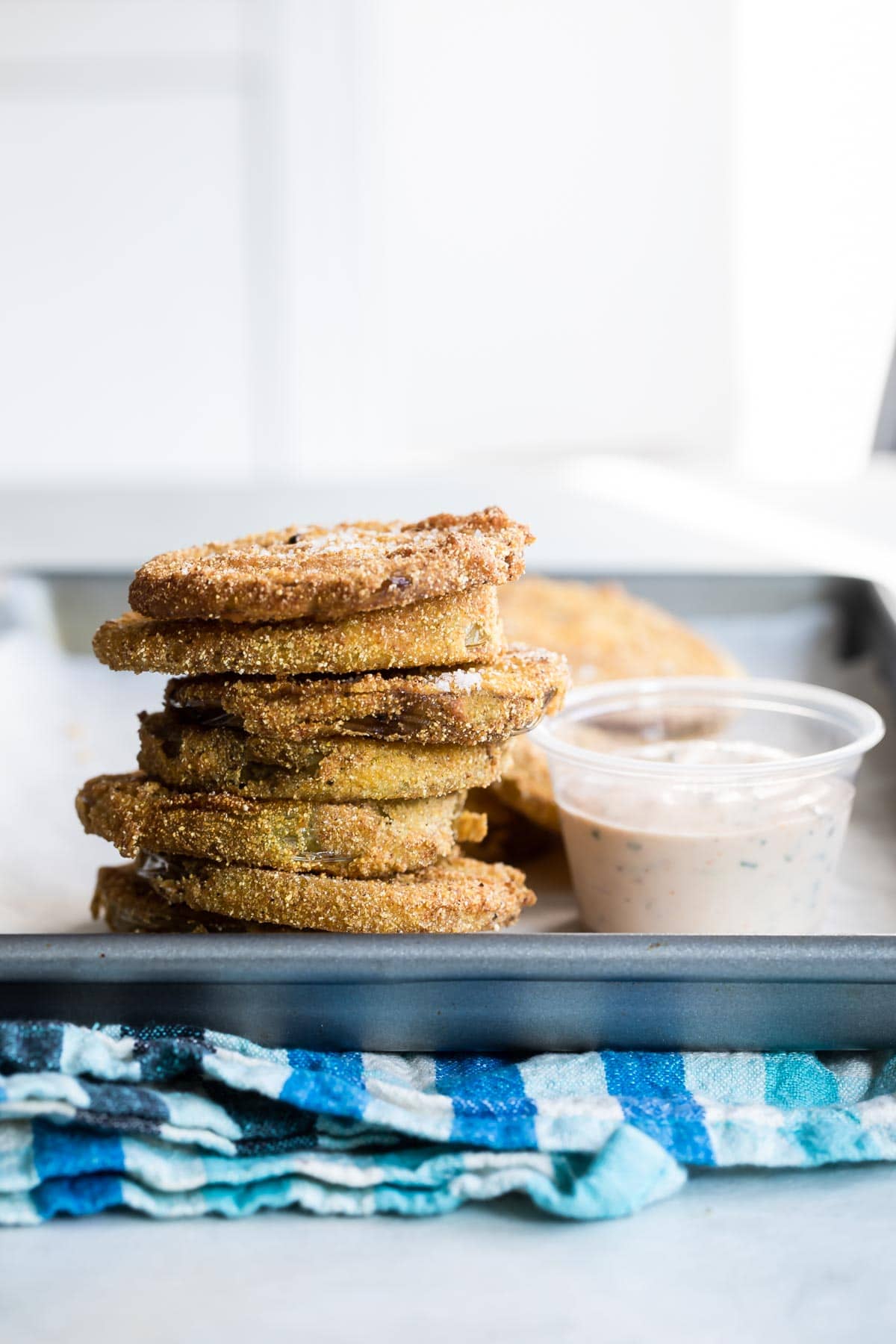 Fried green tomatoes stacked on a sliver tray with a side of remoulade sauce.