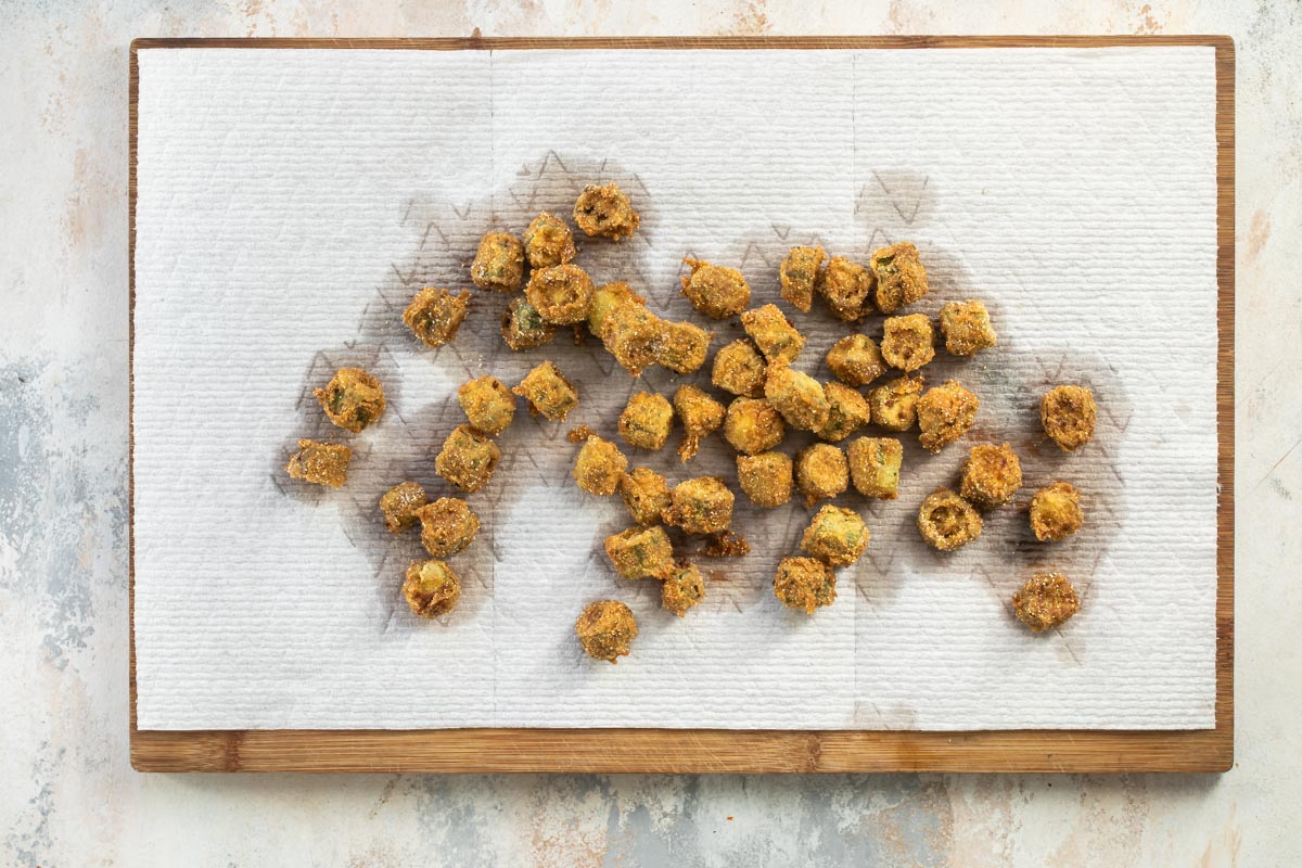 Fried okra on a paper towel lined wooden cutting board.