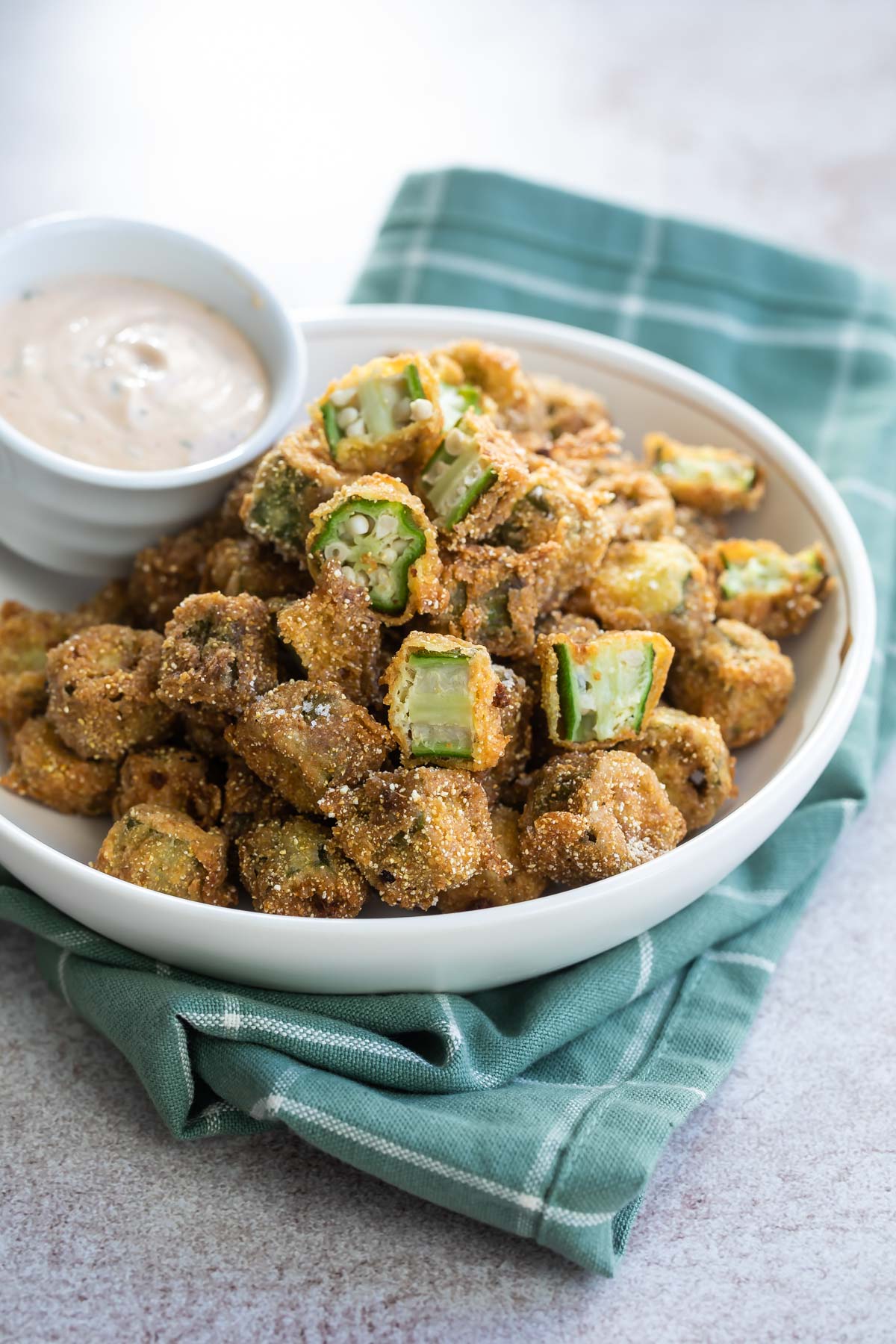 A bowl of fried okra with remoulade sauce on the side.