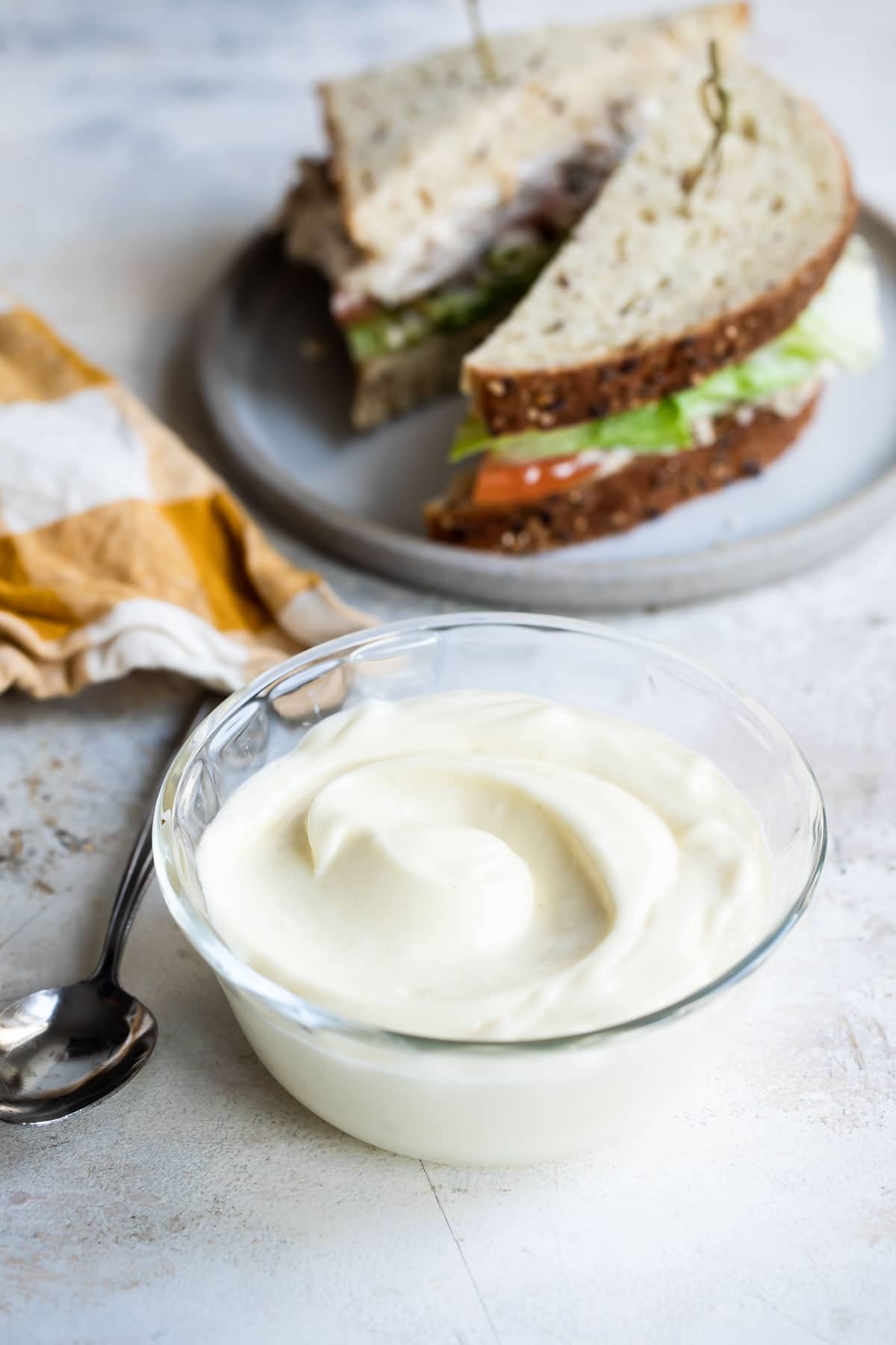 Mayonnaise in a clear bowl with a sandwich in the background.