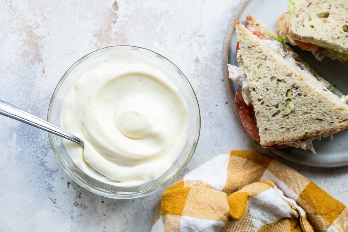 Mayonnaise in a clear bowl next to a sandwich.