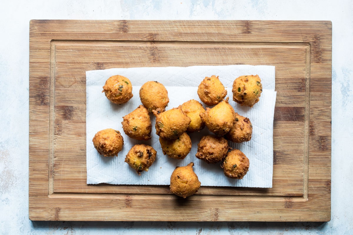 Hush puppies resting on a paper towel on a wooden cutting board.