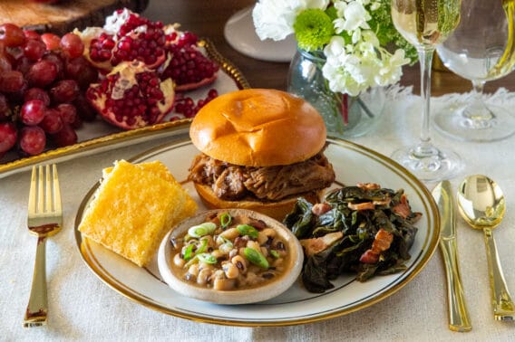 A table set for New Year's Day. A plate with lucky foods like pulled pork, Hoppin' John, collard greens, and cornbread.